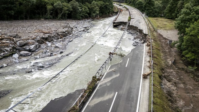 Überfluteter Fluss neben beschädigter Strasse durch Erdrutsch.