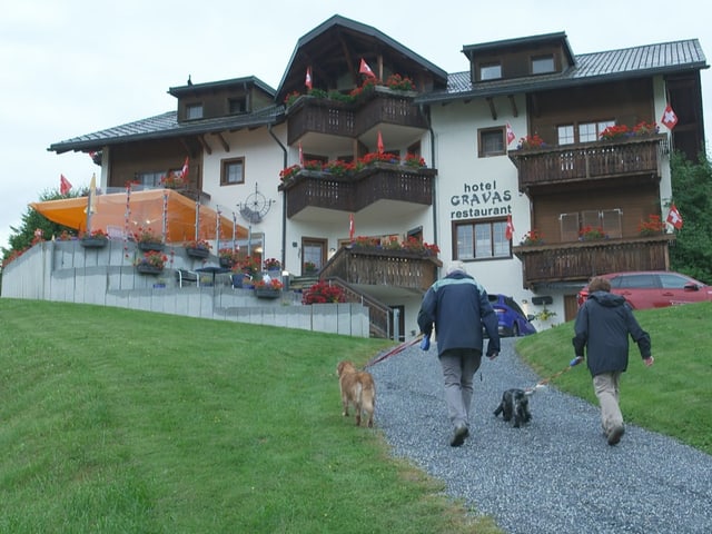 Zwei Personen führen Hunde vor einem Hotel.