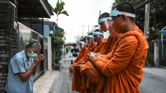  Buddhistische Mönche sammeln Almosen mit Gesichtsschutz. 