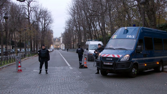 Kastenwagen der Polizei rechts, leere Strasse, ein Polizist steht auf dem Fahrstreifen.