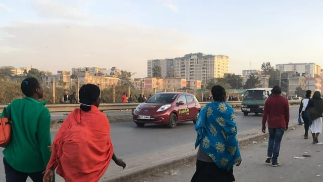 Menschen zu Fuss unterwegs zur Arbeit. Links kommen Autos entgegen