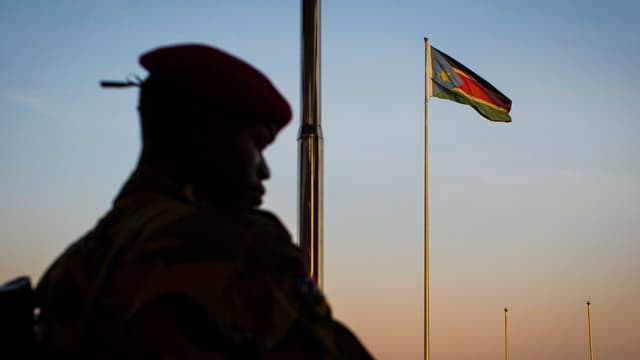 Ein Soldat steht vor einer Fahnenstange, an der eine südsudanesische Flagge weht.