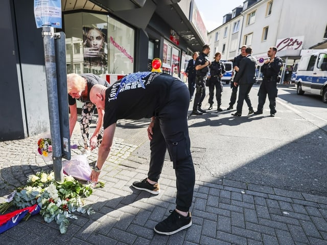 Menschen legen Blumen in einer Stadt nieder; Polizisten im Hintergrund.