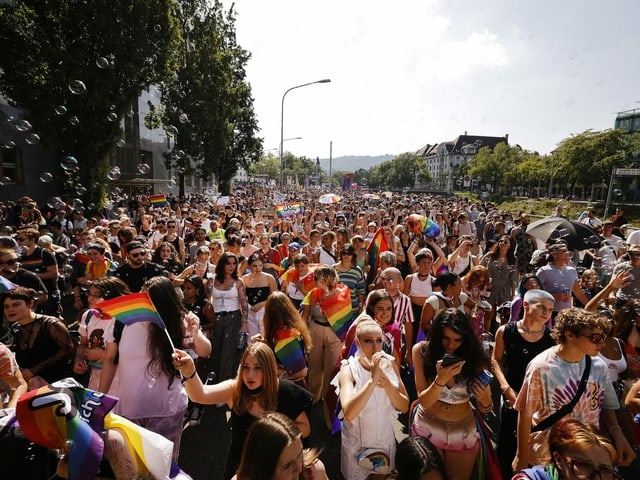 Menschen laufen an einer Demonstration. Halten Regenbogenfahnen hoch.