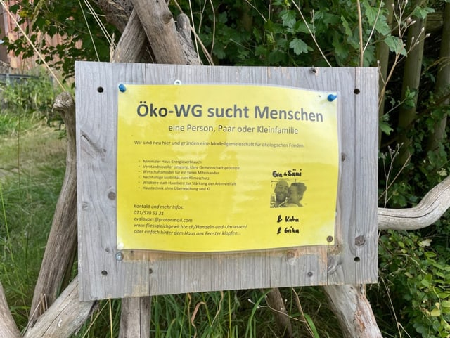 Ein gelbes, laminiertes Blatt ist an einer Holztafel ausgehängt. Neue Mitbewohner:innen werden gesucht.