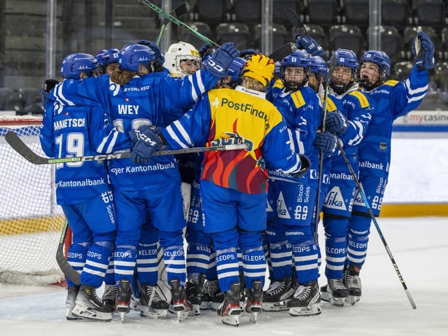 Eishockeymannschaft in blauen Trikots feiert auf dem Eis.