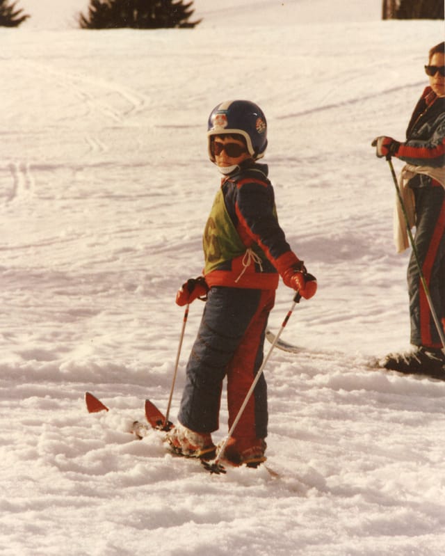 Ein Junge mit Helm und Skikleidung steht auf zwei Skiern im Schnee.