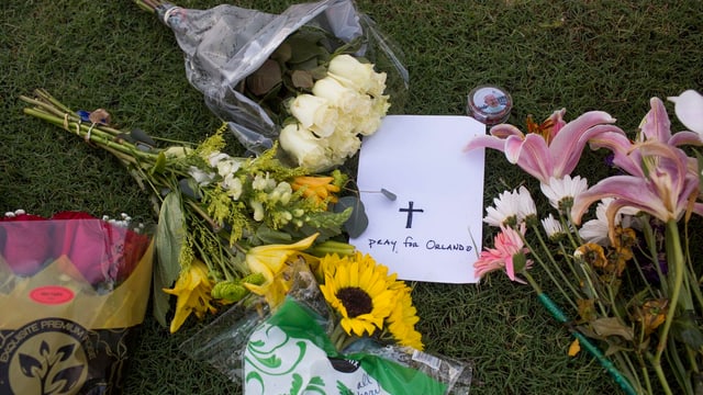 Blumensträusse auf Gras, ein zettel, auf dem Steht «pray for Orlando».