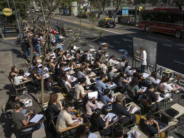 Unterricht im Freien auf Bürgersteig mit Tischen und Studenten.