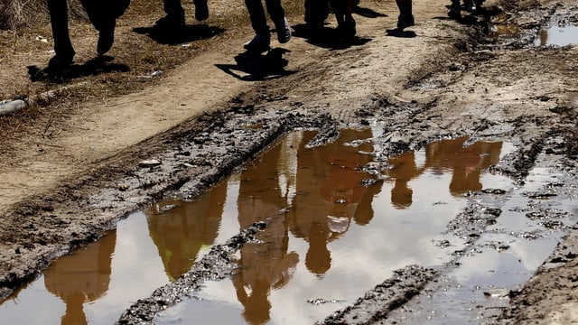 Flüchtlinge in Mazedonien, ihre Silhouette spiegelt sich in einer Wasserpfütze auf einem Trampelpfad. 