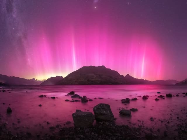 Pinkes Nordlicht über Berg und See bei Nacht.