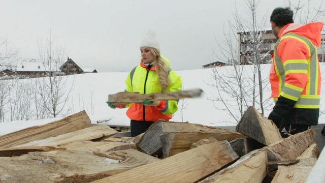 Frau mit Kappe hievt Holz auf einen Anhänger.