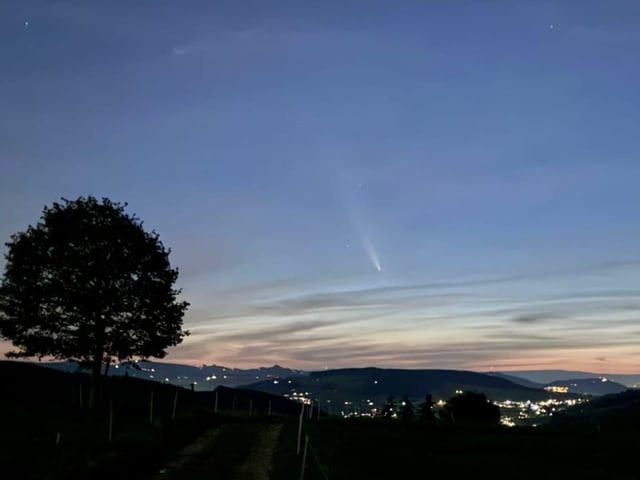 Nächtlicher Himmel mit Komet über beleuchteter Stadt und Hügeln.