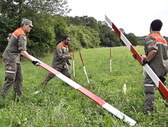 Drei Männer des Zivilschutzes bauen auf einer Wiesenfläche mit Brettern eine Falle.