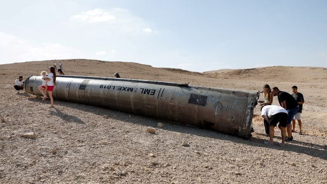 Menschen betrachten liegendes Metallobjekt in Wüstenlandschaft.