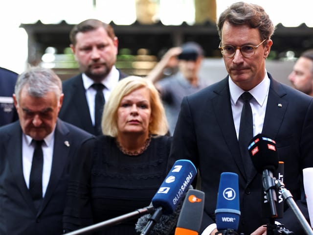 Menschen in formeller Kleidung bei einer Pressekonferenz.