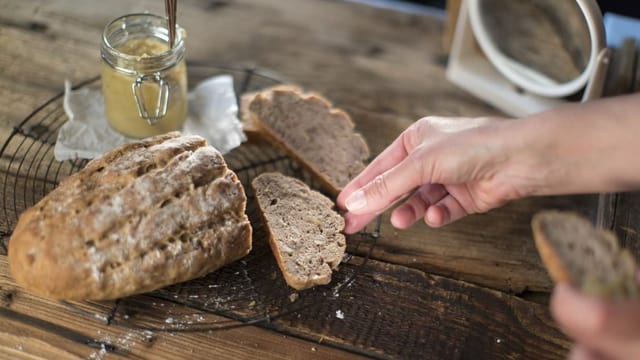 Auf dem Bild ist ein Brot zu sehen. Eine Hand greift nach einem Stück.