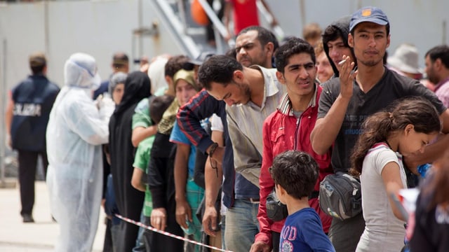 Flüchtlinge in einer Schlange vor einem italienischen Militärschiff