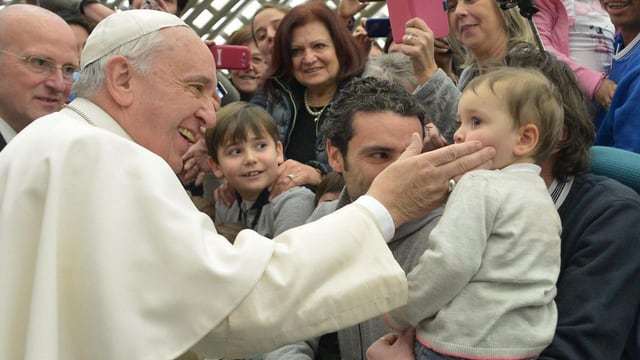 Papst Franziskus tätschelt einem Kind die Wange