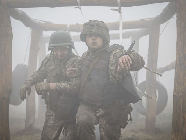 Zwei Soldaten in Tarnkleidung im Nebel, einer stützt den anderen.