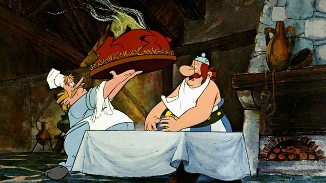 Ein Koch stellt Obelix einen grossen Braten auf den Tisch.