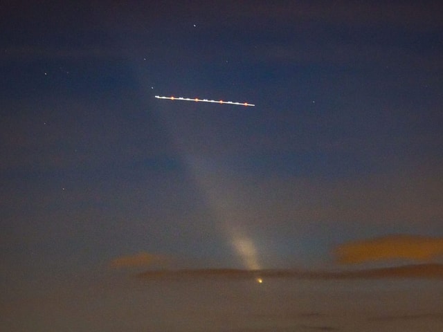 Himmel mit Komet und Flugzeugspuren bei Nacht.