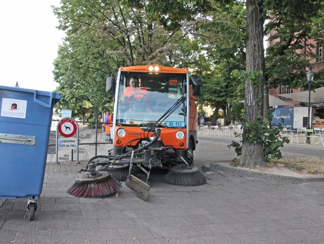 Ein oranger Putzwagen fährt herum.