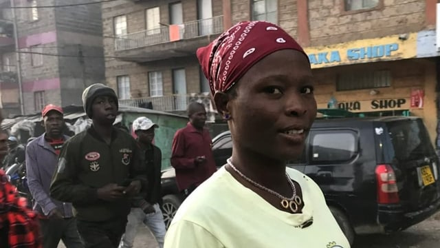 Hellen Achayo, eine junge Frau mit gelbem Shirt und dunkelrotem Kopftuch, schaut leicht lächelnd in die Kamera.