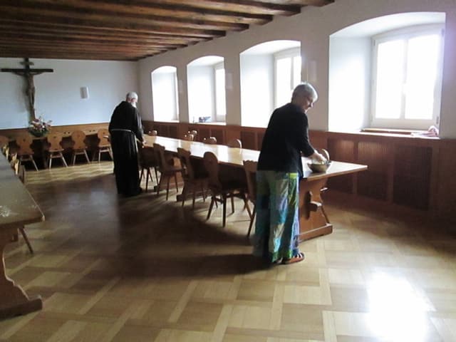 Ein Mann in Mönchskutte und eine Frau im Speisesaal des Klosters.