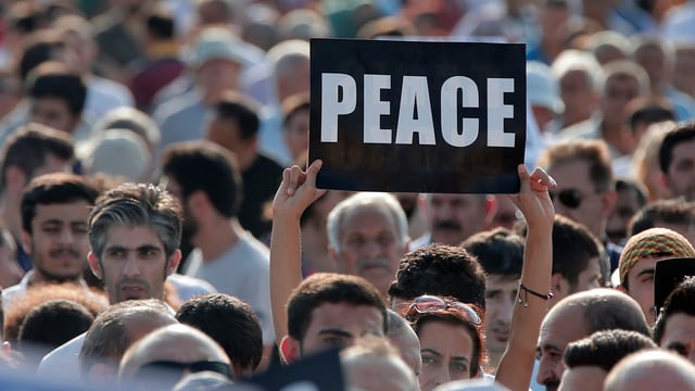 Demonstrant hält Schild mit Schriftzug «Peace» hoch 