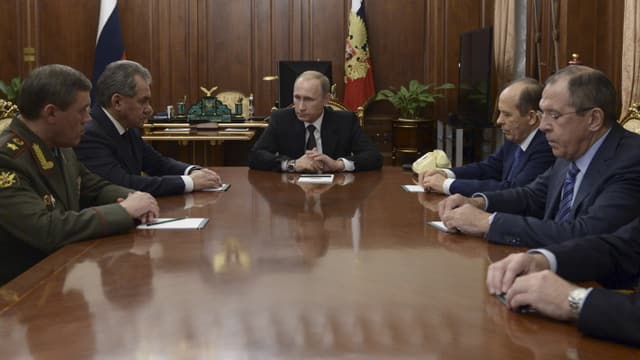 Putin sitzt am Kopf eines Tisches, mehrere Männer in Anzug oder Uniform sitzen links und rechts von ihm.