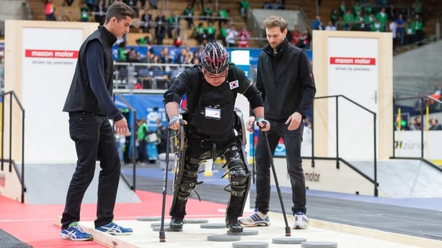 Ein Mann mit Lähmung geht mit Hilfe eines Exoskeletts ein paar gezielte Schritte.