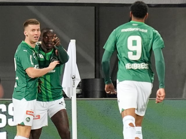 Drei Fussballspieler im grünen Team-Trikot auf dem Spielfeld.