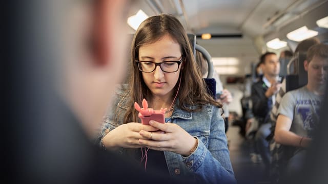 Junge Frau töggelt im vollbesetzten Zug auf ihrem Handy herum