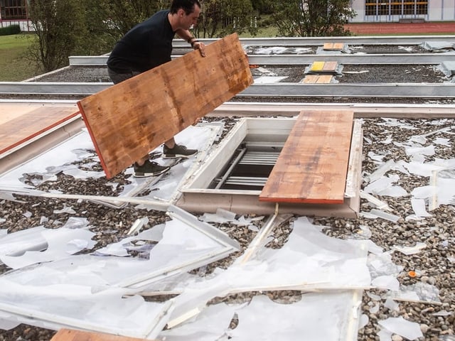 Mann entfernt Holzplatte von Zugangsluke auf Kiesdach.