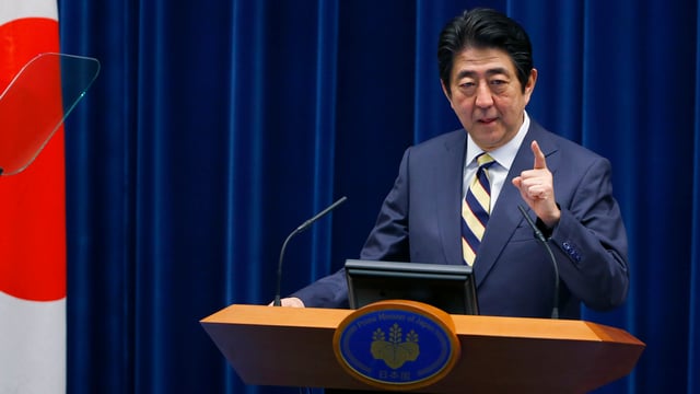 Japans Ministerpräsident Shinzo Abe neben einer japanischen Flagge an einem Rednerpult.