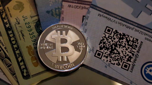 Eine Bitcoin-Münze, daneben Dollarscheine und ein Zertifikat für Bitcoins.