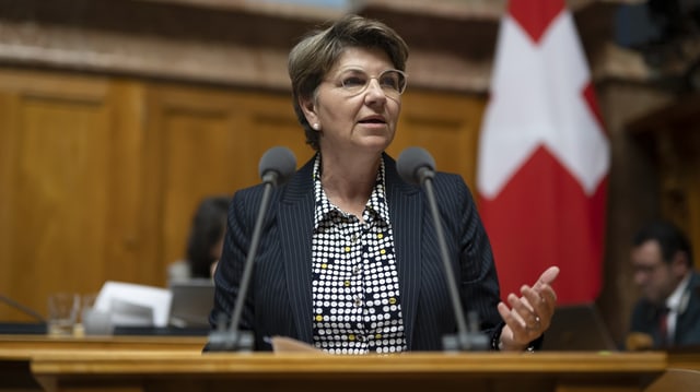 Viola Amherd spricht. Brille, kurzes Haar, gestikulierend. Zwei Mikrofon vor ihr, im Hintergrund die Schweiz-Flagge.