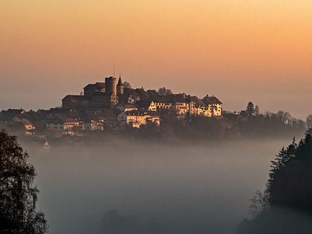 Ein Hügel mit Burg ragt aus dem Nebel empor.