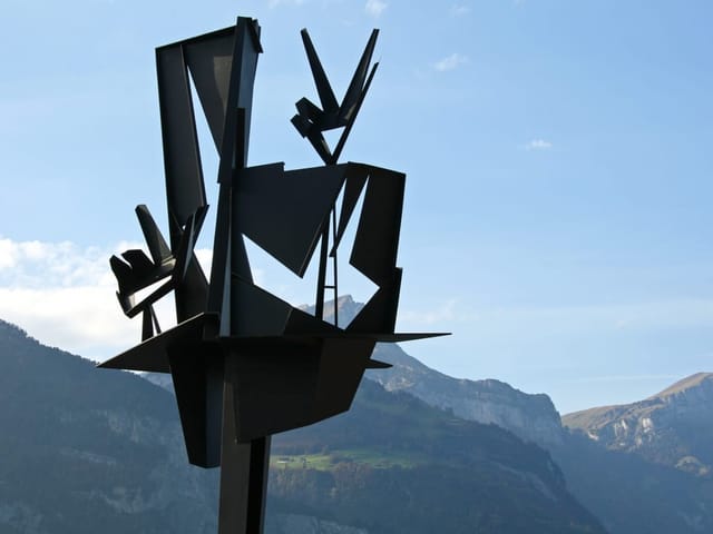 Abstrakte schwarze Skulptur vor Bergkulisse.