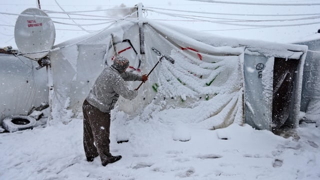 Ein Mann klopft Schnee von seinem Zelt in einem Flüchtlingslager. 