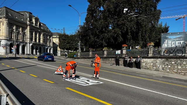 Orange gekleidete Männer malen eine 30 auf den Boden.