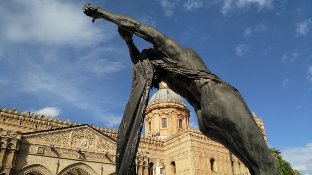 Ein Statue einer Frau. Im Hintergrund eine Kathedrale mit grosser Kuppel.