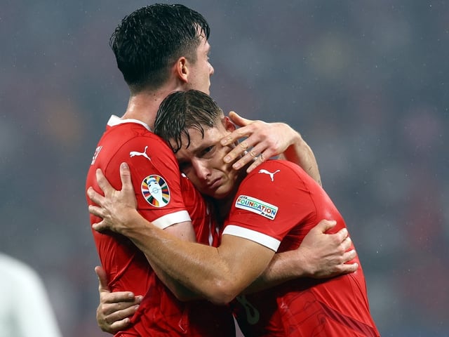 Zwei Fussballspieler in roten Trikots umarmen sich auf dem Spielfeld.