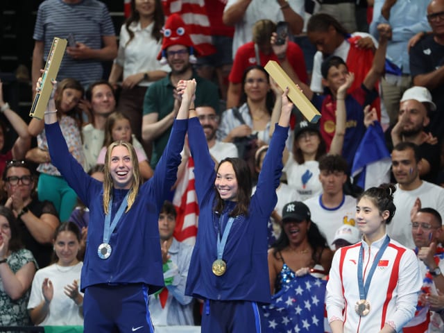 Zwei gefeierte Athletinnen mit Medaillen und Trophäen, eine weitere Athletin daneben.