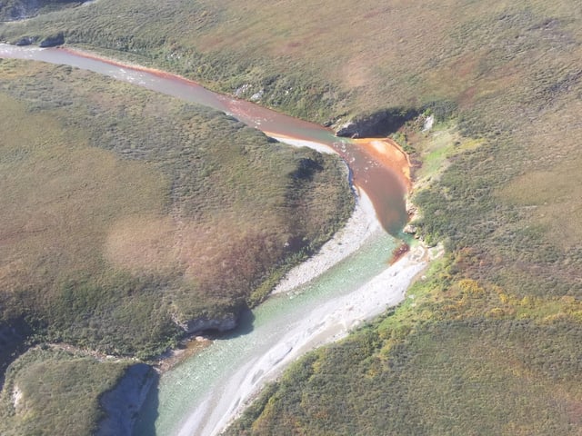 Ein Fluss mit orange-Färbung fliesst durch eine Landschaft.