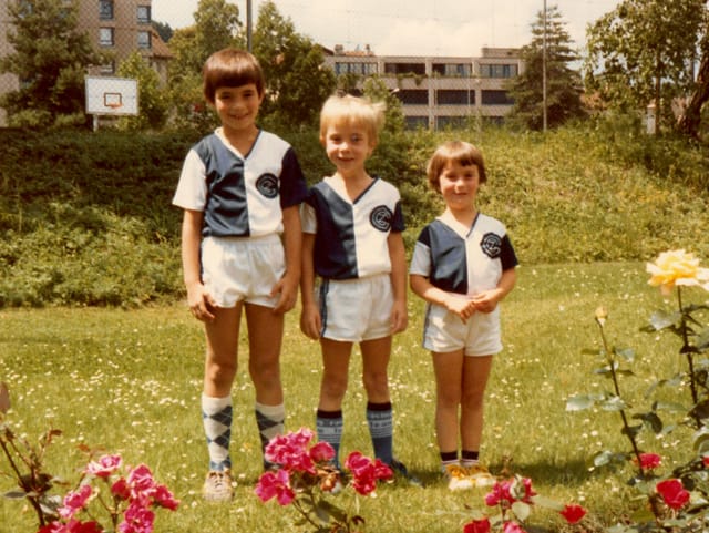 Drei Kinder in identischem Fussballtrikot auf Wiese. 