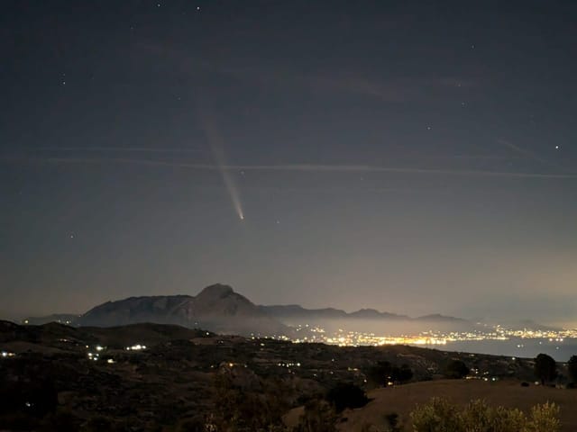 Komet am Nachthimmel über einer beleuchteten Stadtlandschaft.