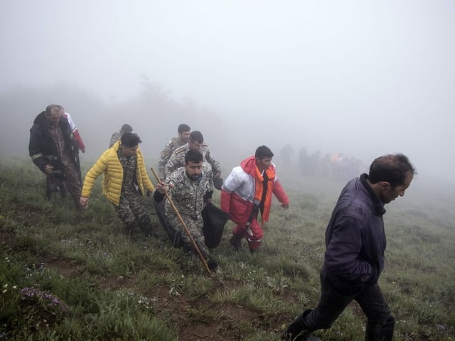 Menschen, die bei Nebel einen grasbewachsenen Hügel hinaufgehen.