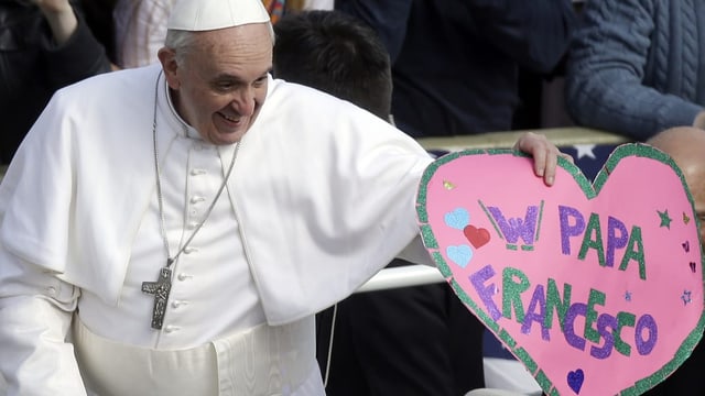 alter Mann in weisser Kutte und weissem Käppchen, hält pinkes Papierherz mit «Papa Francesco».